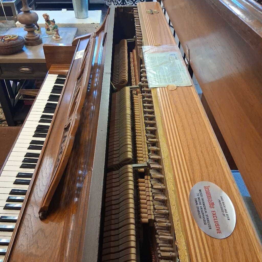 Wooden piano with open lid showing internal mechanism, surrounded by a room setting.