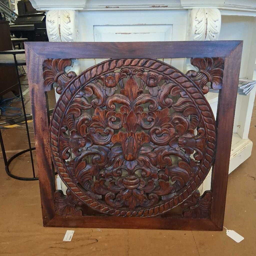 Decorative wooden panel with intricate carvings on a brown surface.