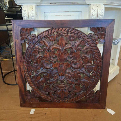 Decorative wooden panel with intricate carvings on a brown surface.
