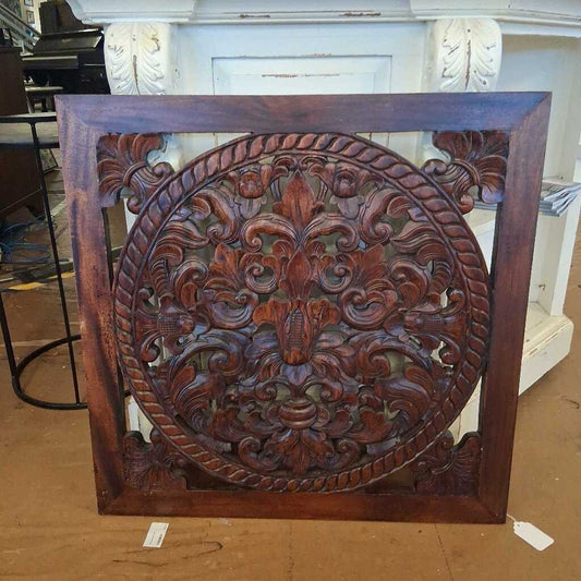 Decorative wooden panel with intricate carvings on a brown surface.
