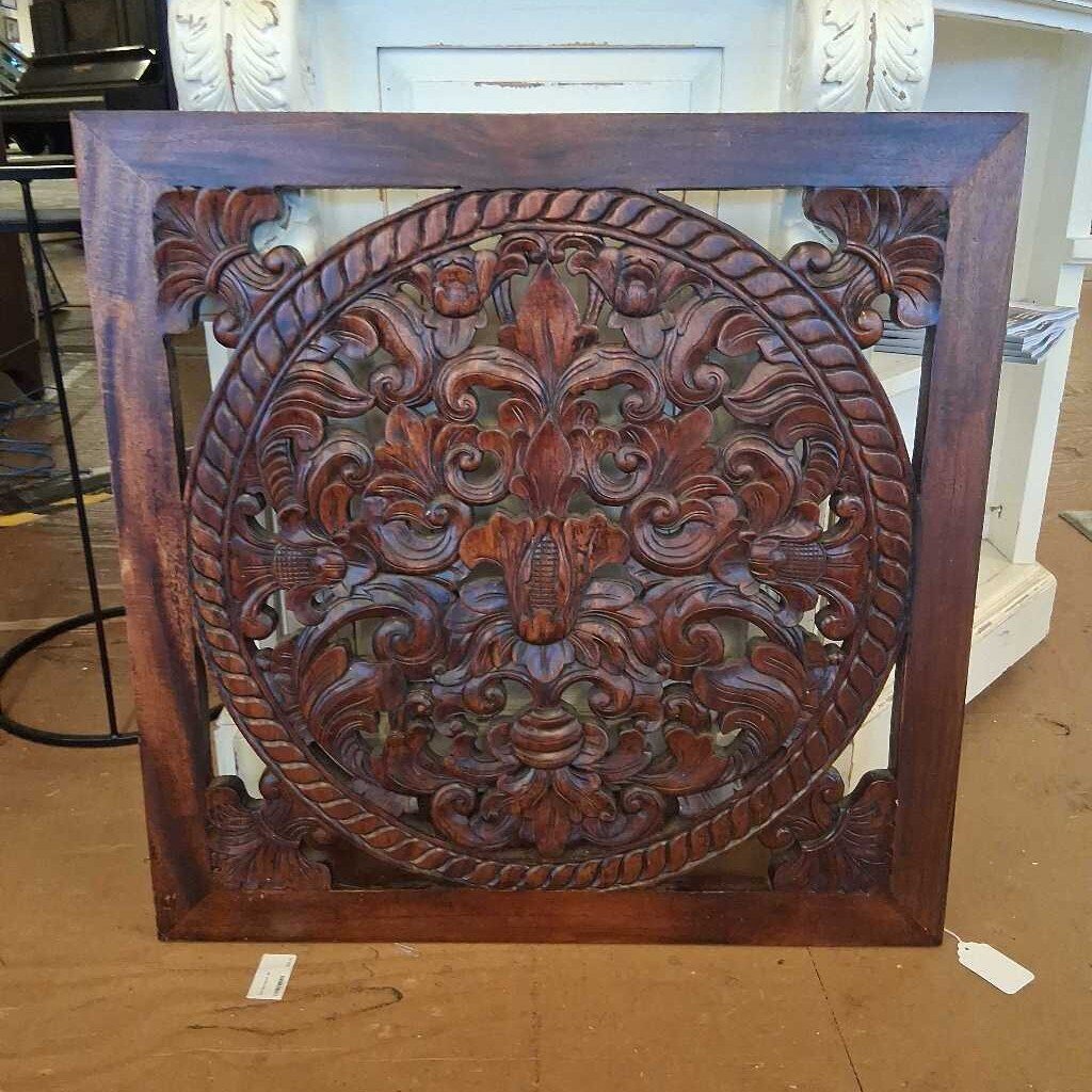 Carved wooden panel with intricate design on a brown surface