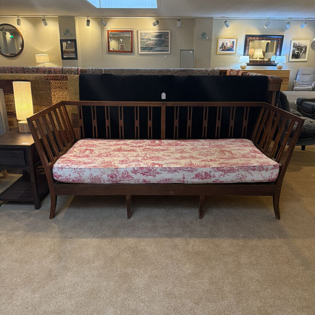 Wooden bench with red and white patterned cushion in a room with framed pictures on the wall.