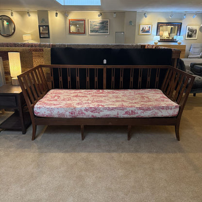 Wooden bench with red and white patterned cushion in a room with framed pictures on the wall.