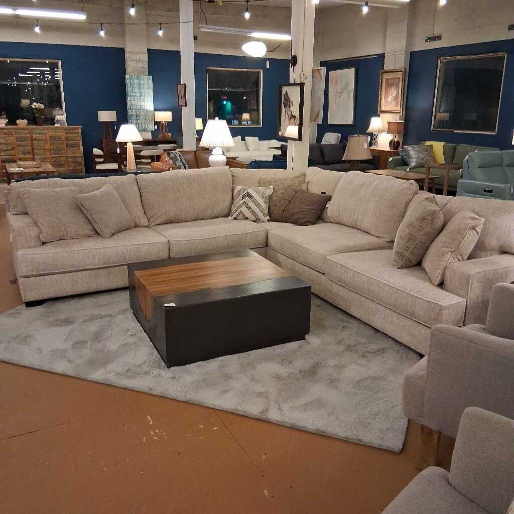 Beige sectional sofa in a showroom with a wooden coffee table and various decor items.