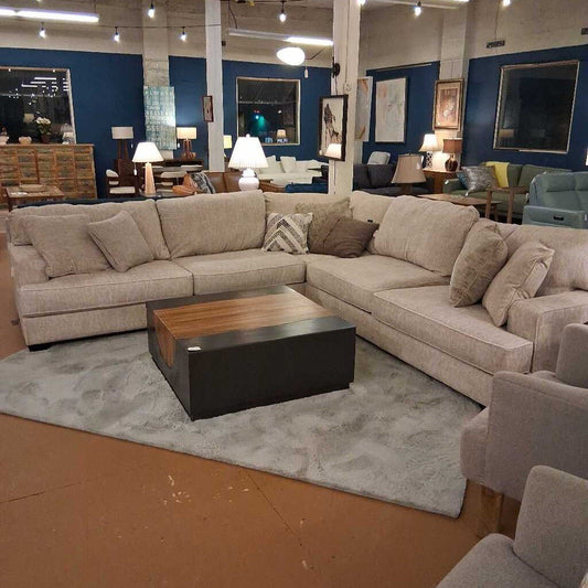 Beige sectional sofa in a showroom with a wooden coffee table and various decor items.