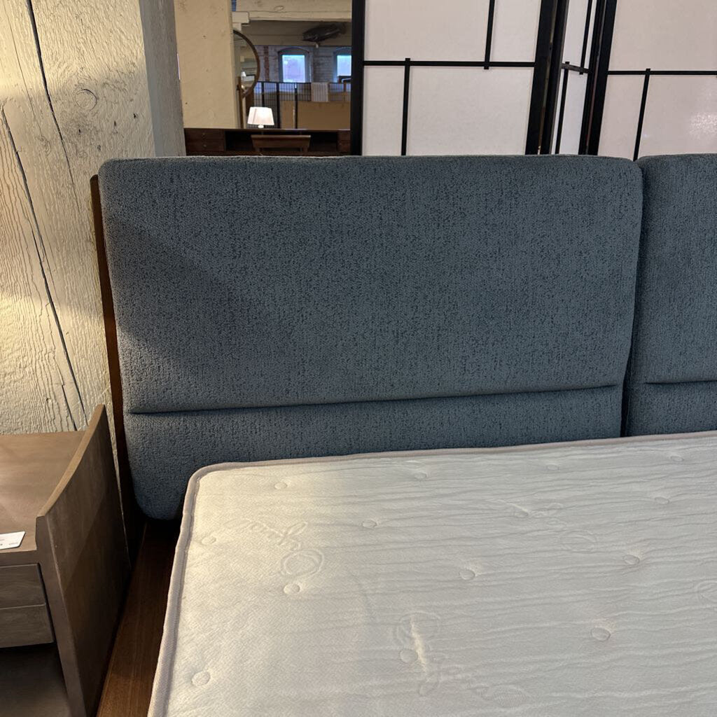 Gray upholstered bed with a wooden headboard in a room setting.