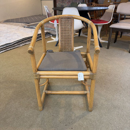 Bamboo chair with a gray cushion on a carpeted floor, surrounded by other furniture.
