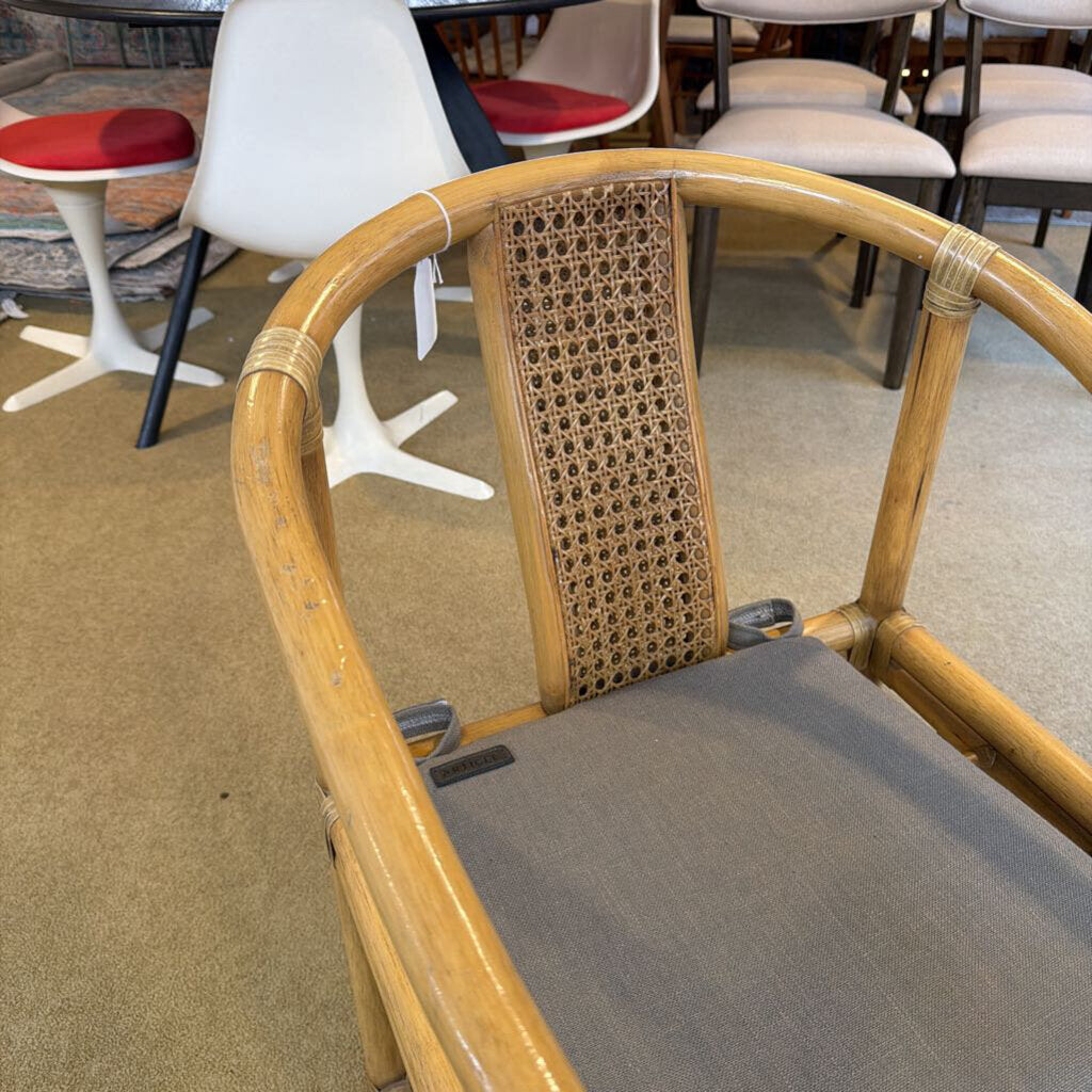 Chair with wicker back and gray cushion in a room with other chairs.