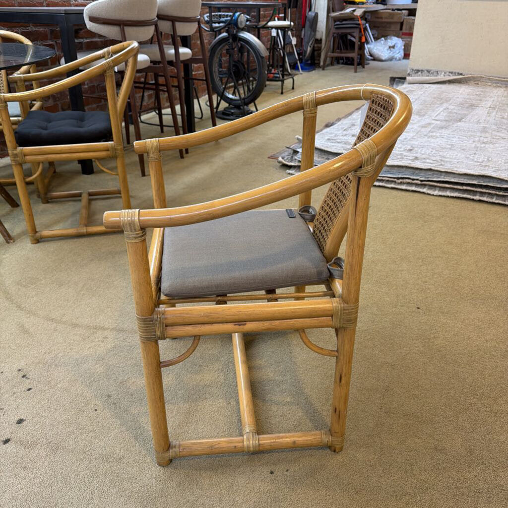 Rattan chair with a gray cushion on a beige floor, surrounded by other furniture.