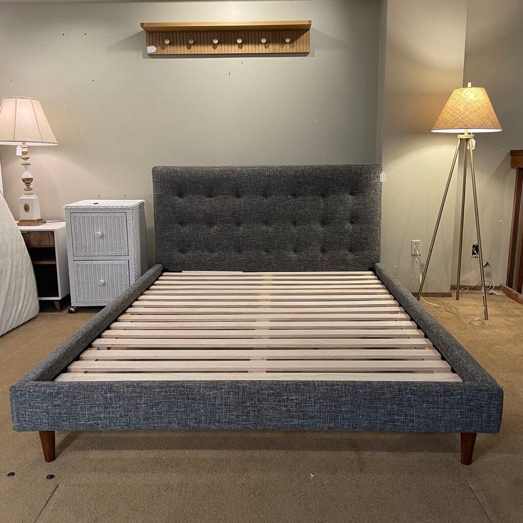 a speckled grey tufted fabric bed frame with blond wooden slats and dark wooden legs