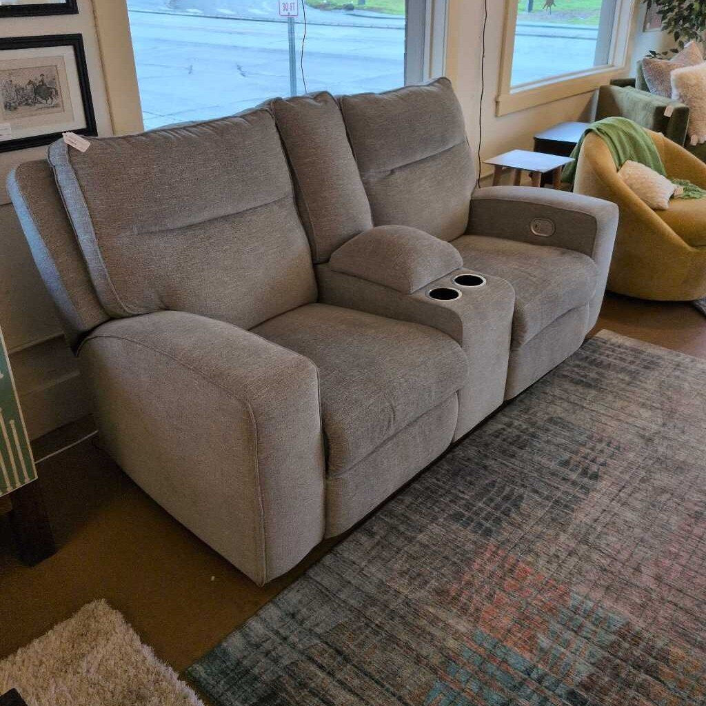 Beige reclining sofa in a living room setting with a rug and window in the background.