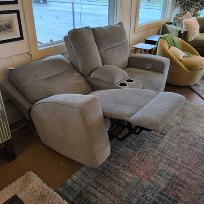 Beige recliner sofa in a living room setting with a rug and window in the background.