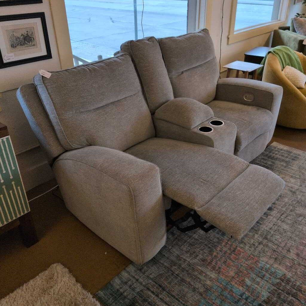 Beige recliner sofa in a living room setting with a rug and wall art.
