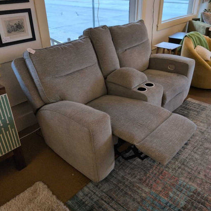 Beige recliner sofa in a living room setting with a rug and wall art.