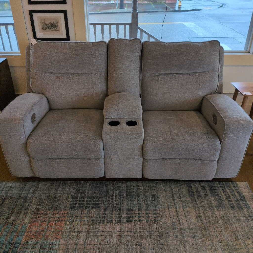 Gray reclining sofa with cup holders in a room with a window and rug.
