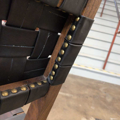 Close-up of a chair with woven leather backrest and wooden frame, featuring brass studs.