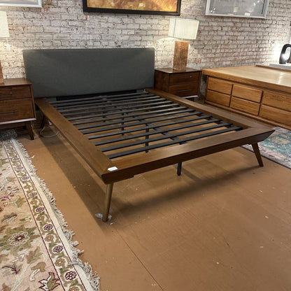 Wooden bed frame in a room with brick walls and furniture.