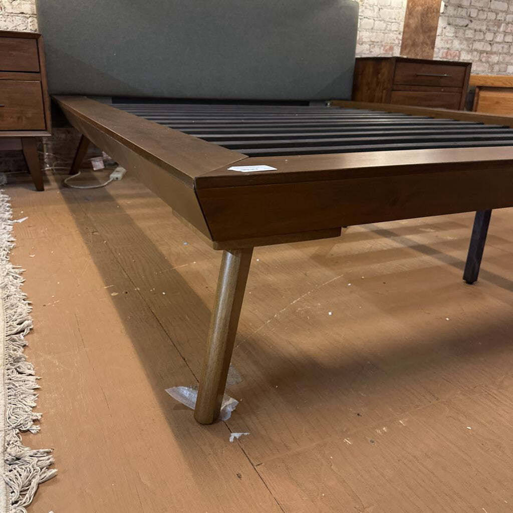 Wooden bed frame on a wooden floor with a brick wall background