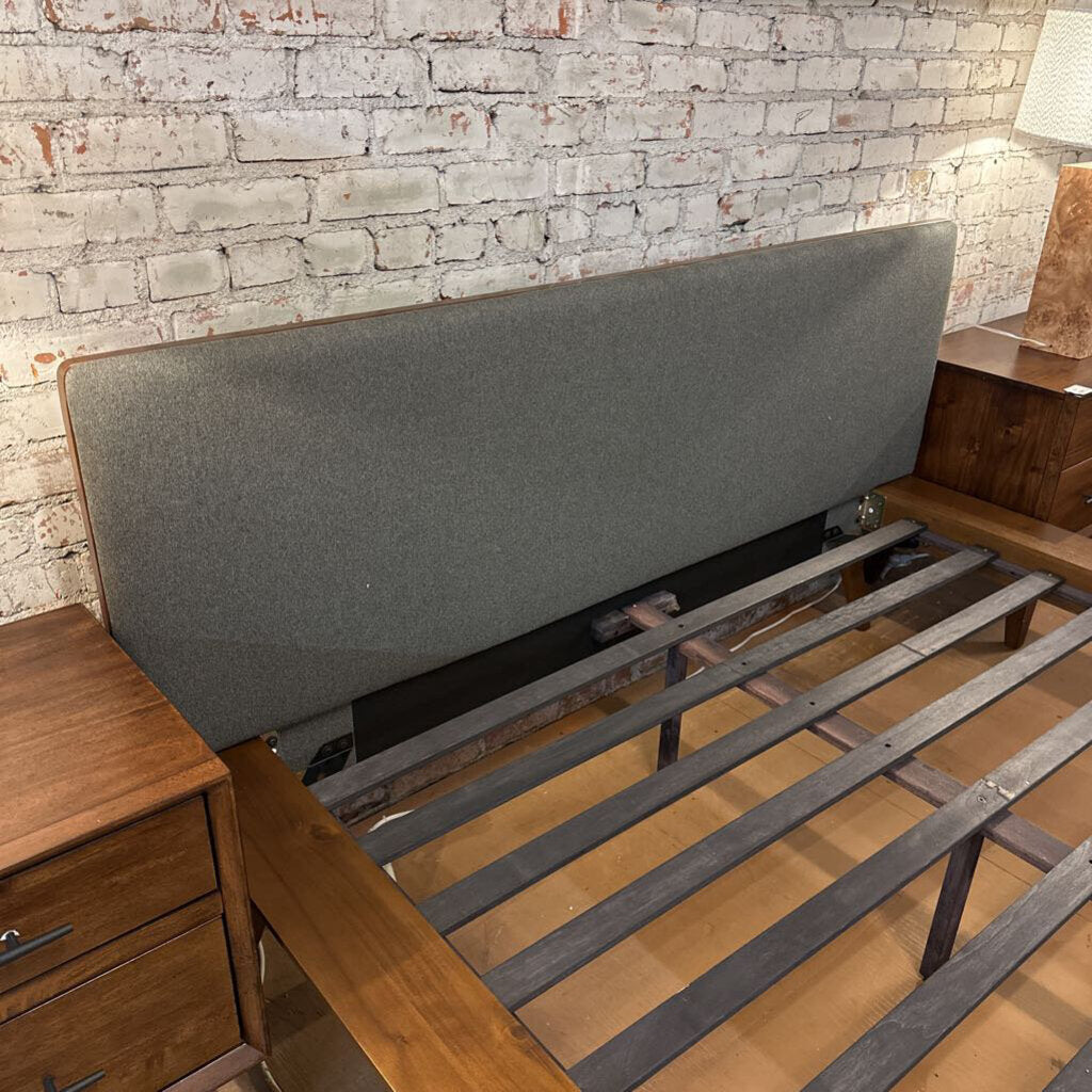 Gray upholstered headboard against a brick wall with wooden furniture.