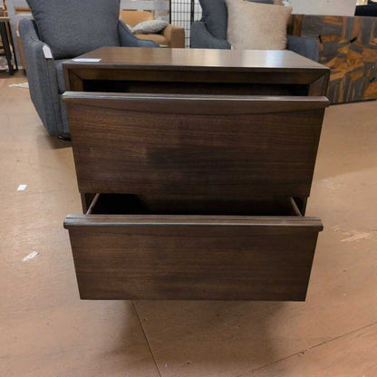 Wooden nightstand with two drawers on a brown floor.
