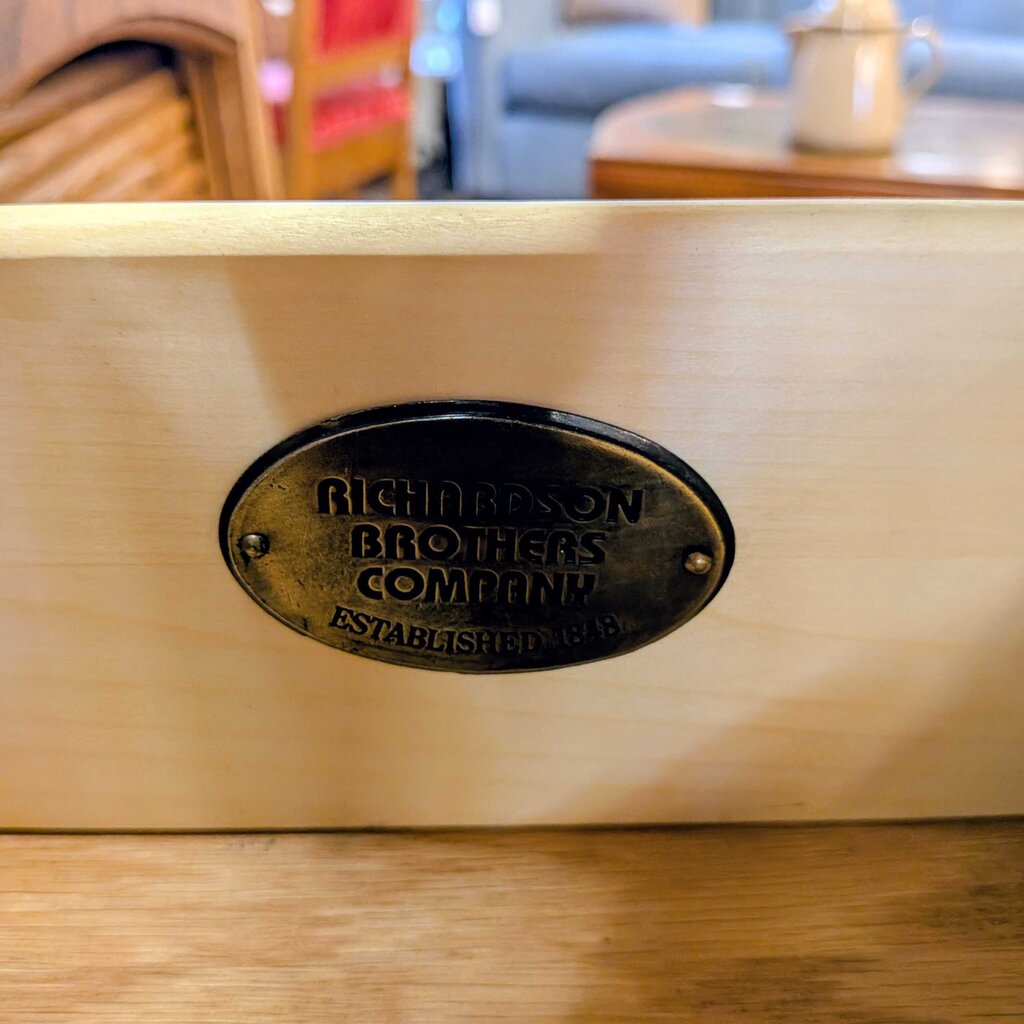 Wooden drawer with Richardson Brothers Company label in a blurred indoor setting