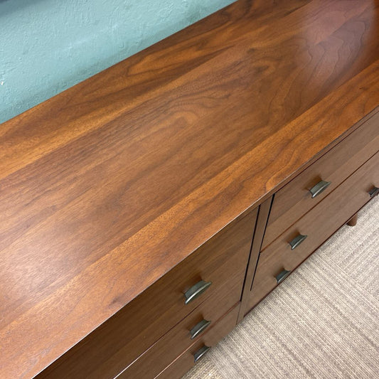 Wooden dresser with drawers and metal handles on a carpeted floor.