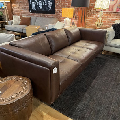 Brown leather sofa in a living room setting with a brick wall and decorative items.