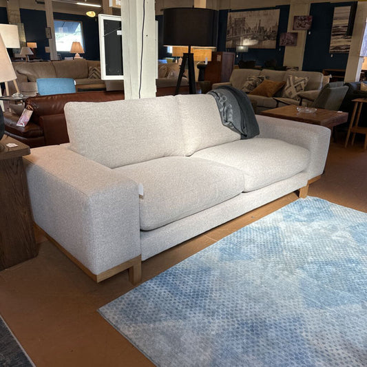 Light gray sofa in a showroom with a blue patterned rug on the floor.