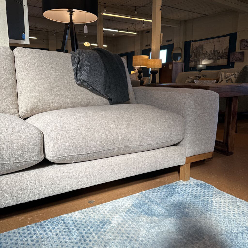 Gray sofa in a store setting with a rug on the floor.
