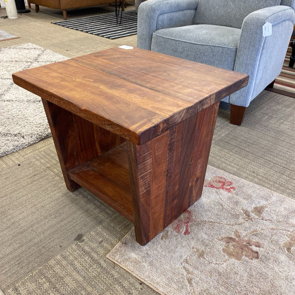 Wooden side table in a room with a gray armchair and patterned rug.