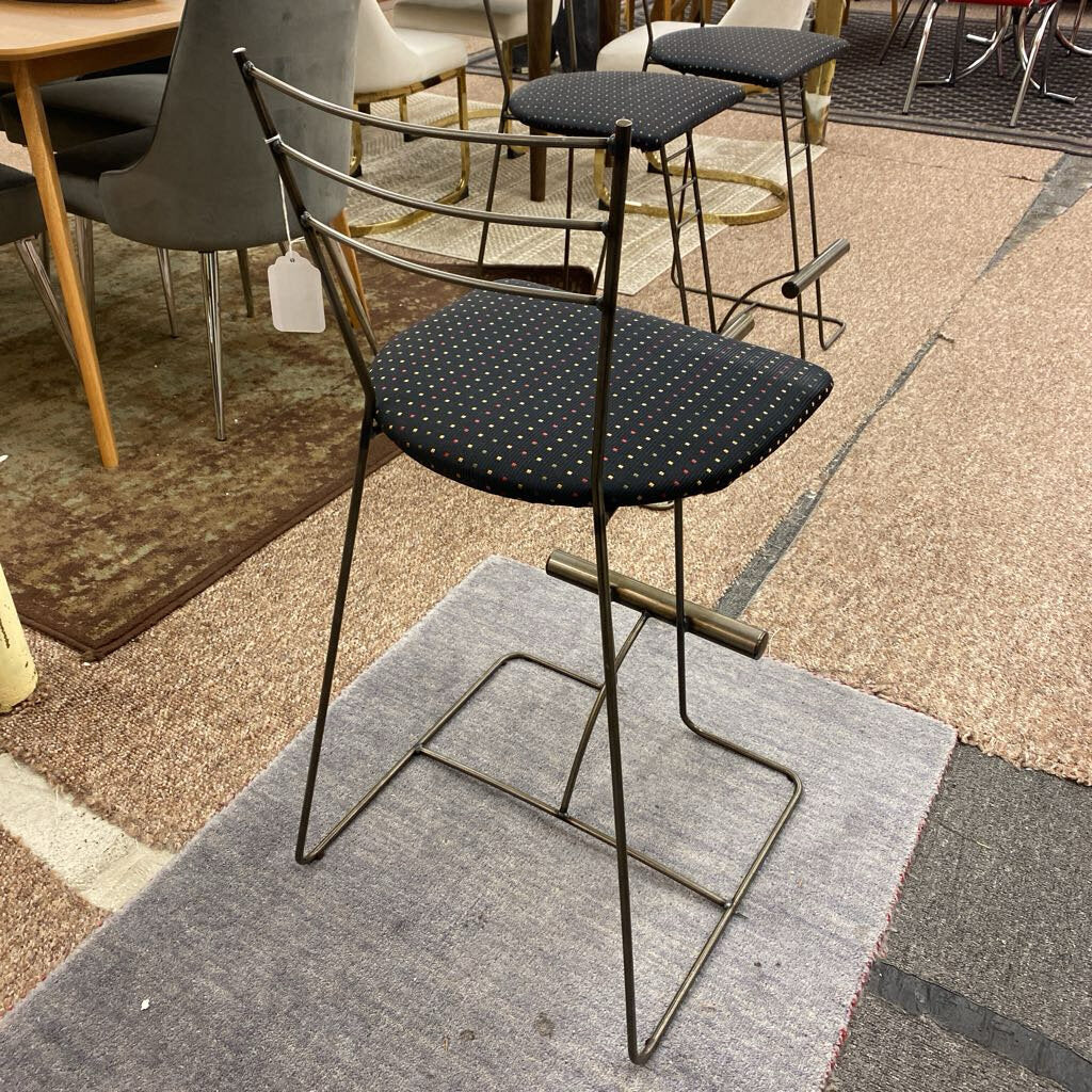 Black bar stool with a metal frame on a gray rug in a showroom setting.