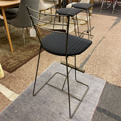 Black bar stool with a metal frame on a gray rug in a showroom setting.