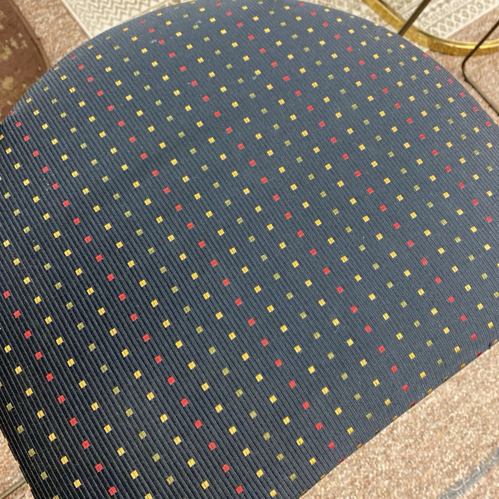 Close-up of a textured fabric with a pattern of small squares in red, yellow, and blue on a dark blue background.