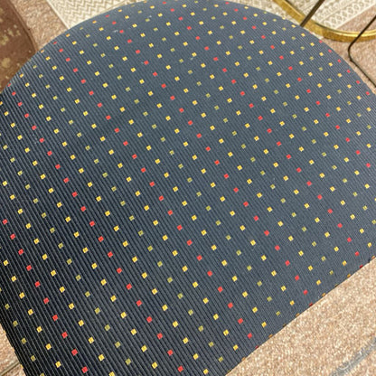 Close-up of a textured fabric with a pattern of small squares in red, yellow, and blue on a dark blue background.