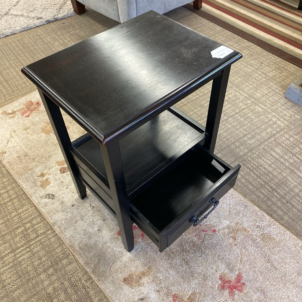 Black side table with a drawer on a patterned carpet