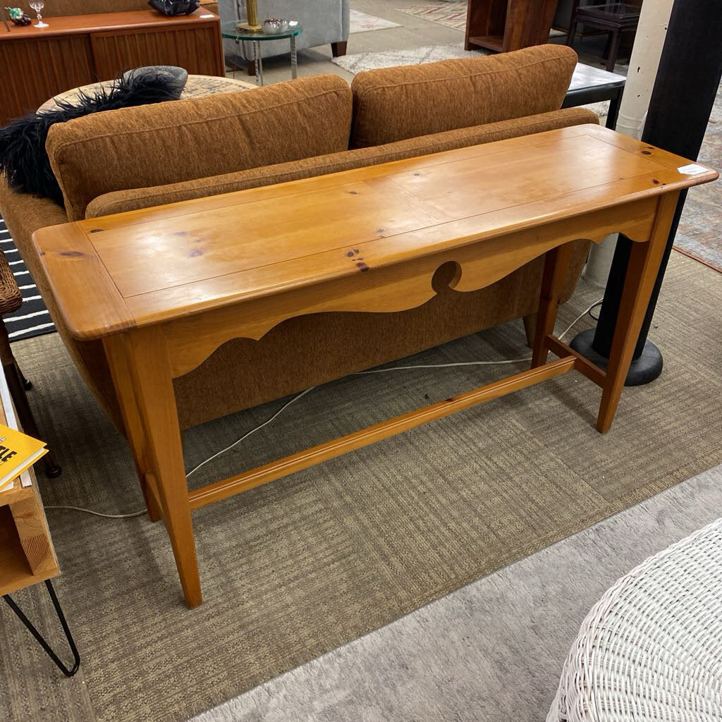 Wooden console table in a furniture store with a brown sofa in the background.