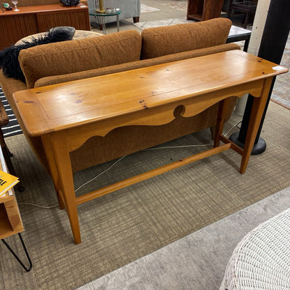 Wooden console table in a furniture store with a brown sofa in the background.