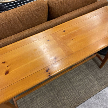 Wooden bench in front of a brown sofa on a carpeted floor