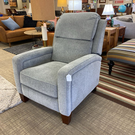 Gray recliner chair in a furniture store setting with other chairs and decor in the background.