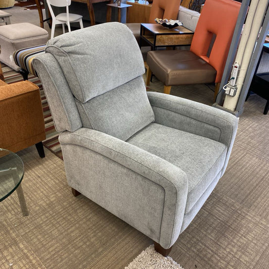 Gray recliner chair in a furniture store setting with other chairs and tables.