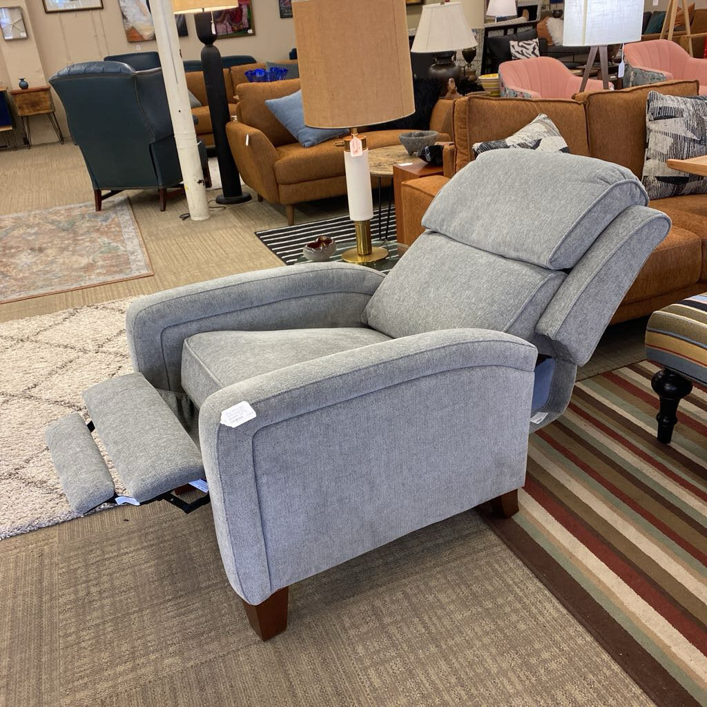 Gray recliner chair in a showroom setting with furniture and decor in the background.