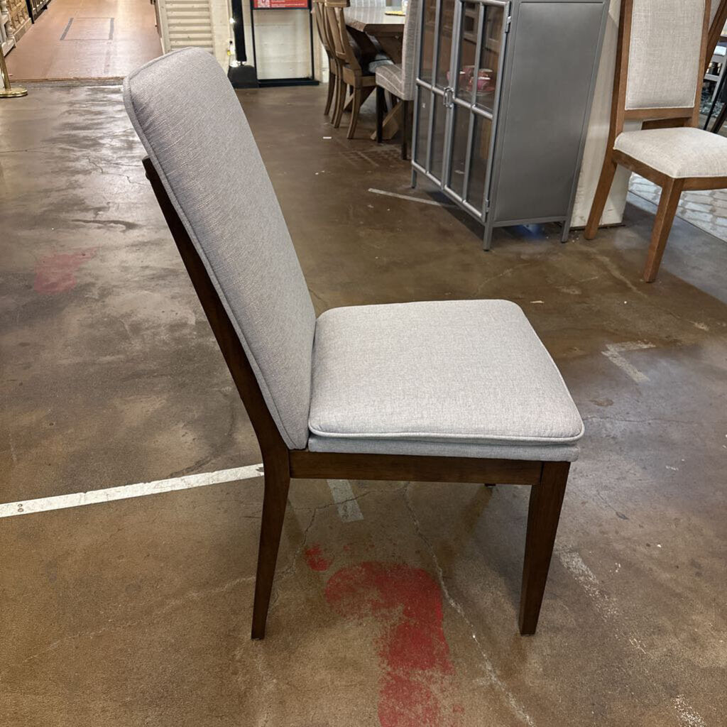 Gray upholstered chair with wooden legs on a concrete floor.