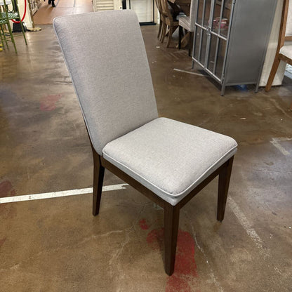 Gray upholstered chair with wooden legs on a brown floor.
