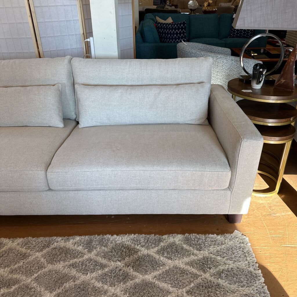 Gray sofa in a living room setting with a rug and lamp visible.