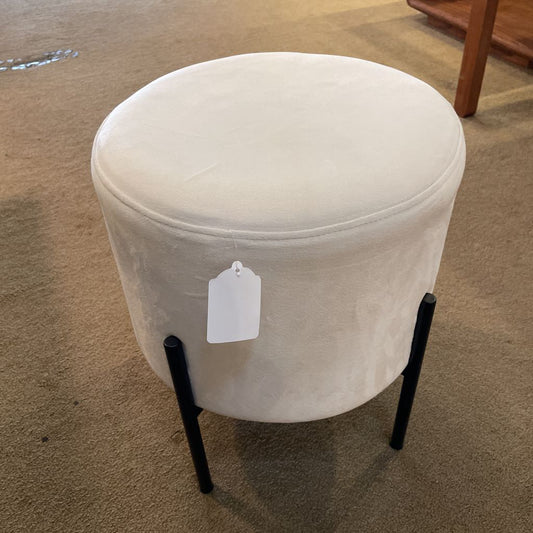White round ottoman with black legs on a carpeted floor