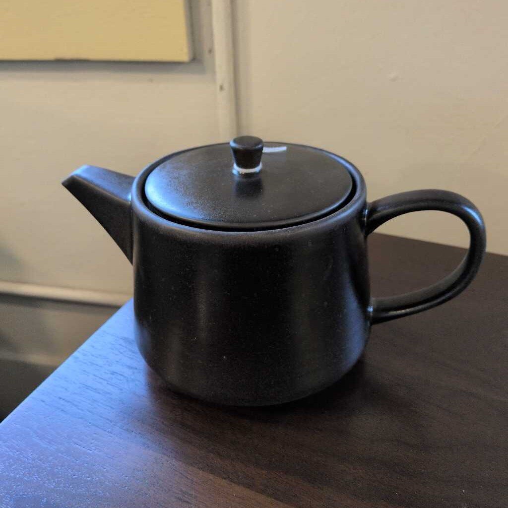 Black teapot on a wooden surface with a neutral background