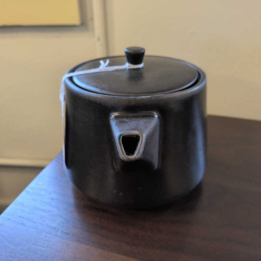 Black ceramic teapot on a wooden surface with a neutral background