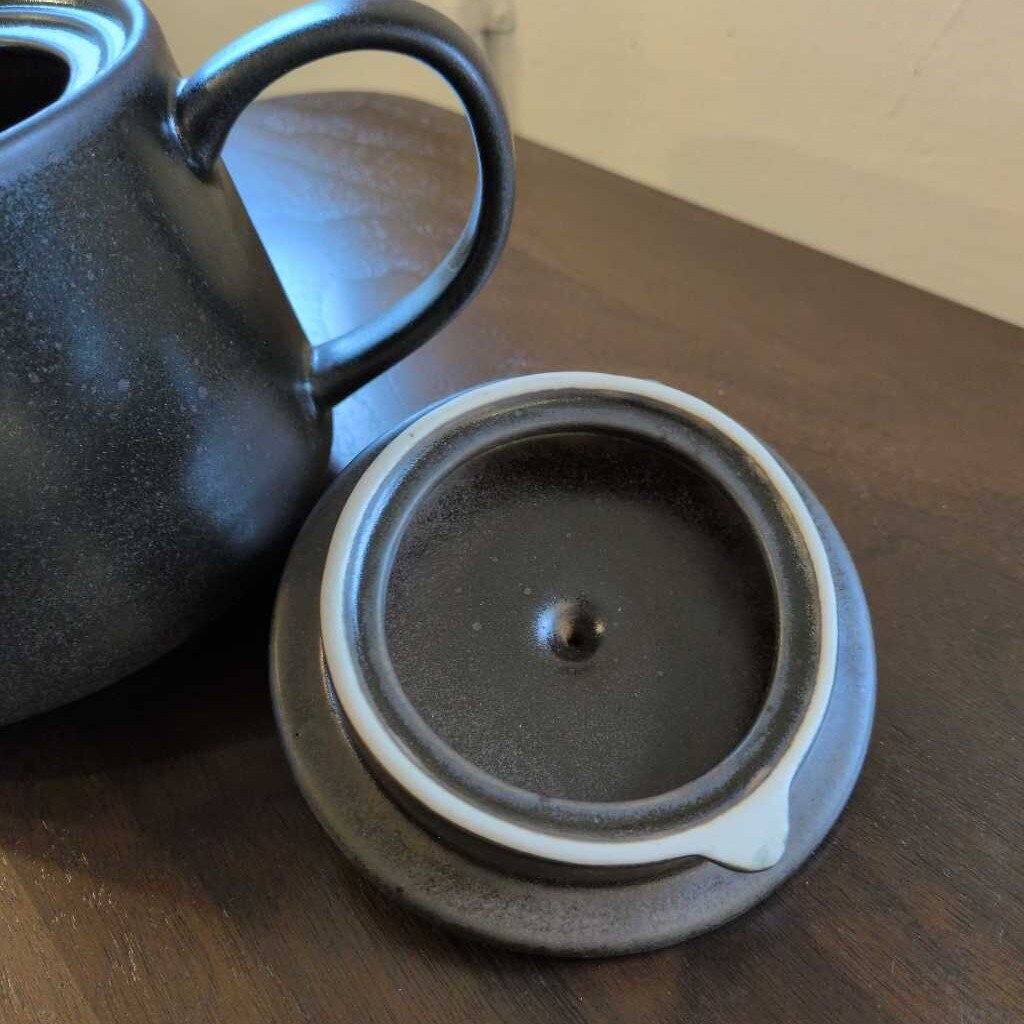 Black ceramic teapot with matching lid on a wooden surface