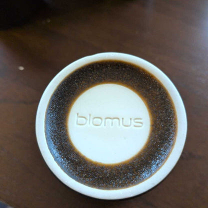 Round white object with 'blomus' branding on a wooden surface