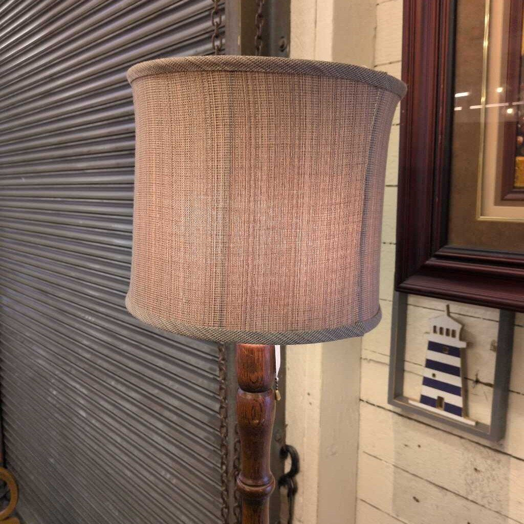 Floor lamp with a textured brown shade against a wall with a framed picture.
